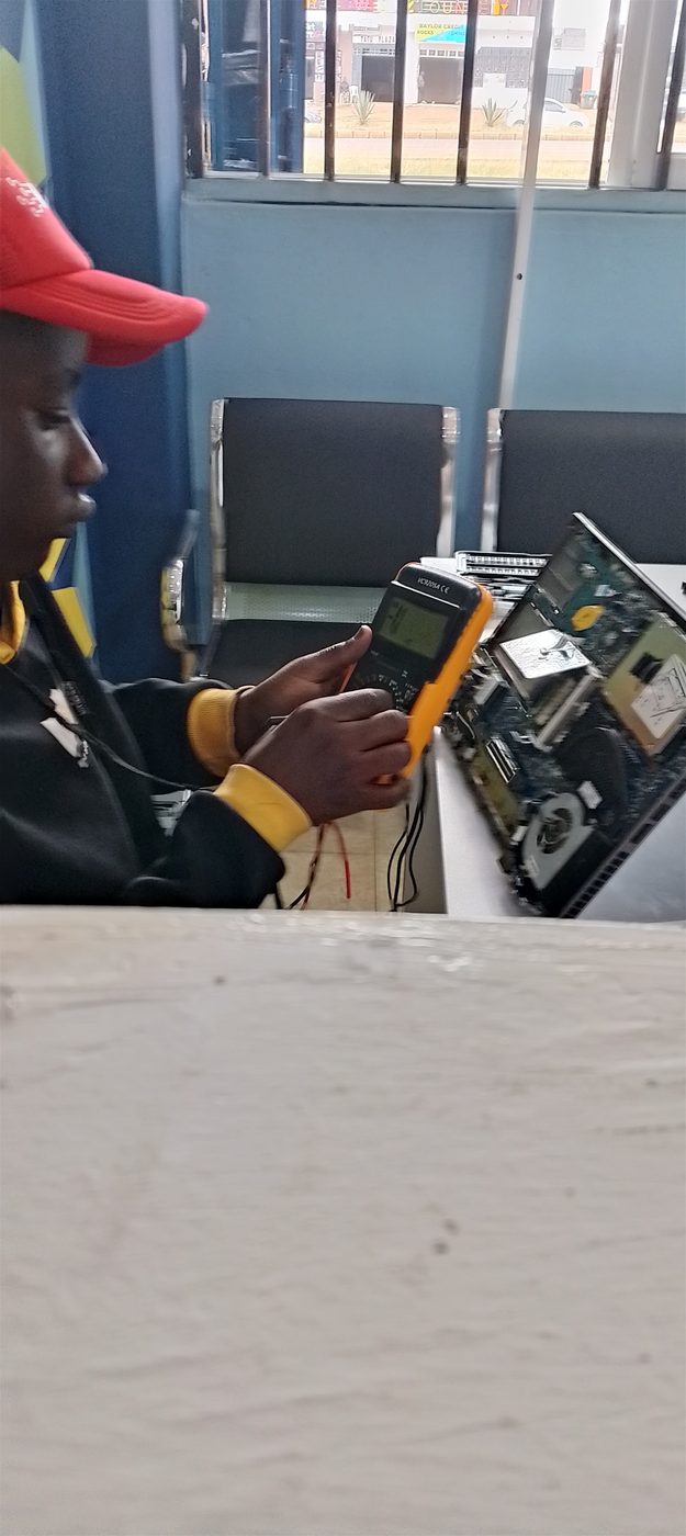 Technician testing a laptop motherboard with a multimeter